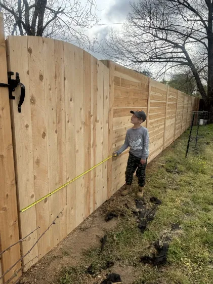 Mike Spencer's son measuring a finished cedar privacy fence in Jackson, TN